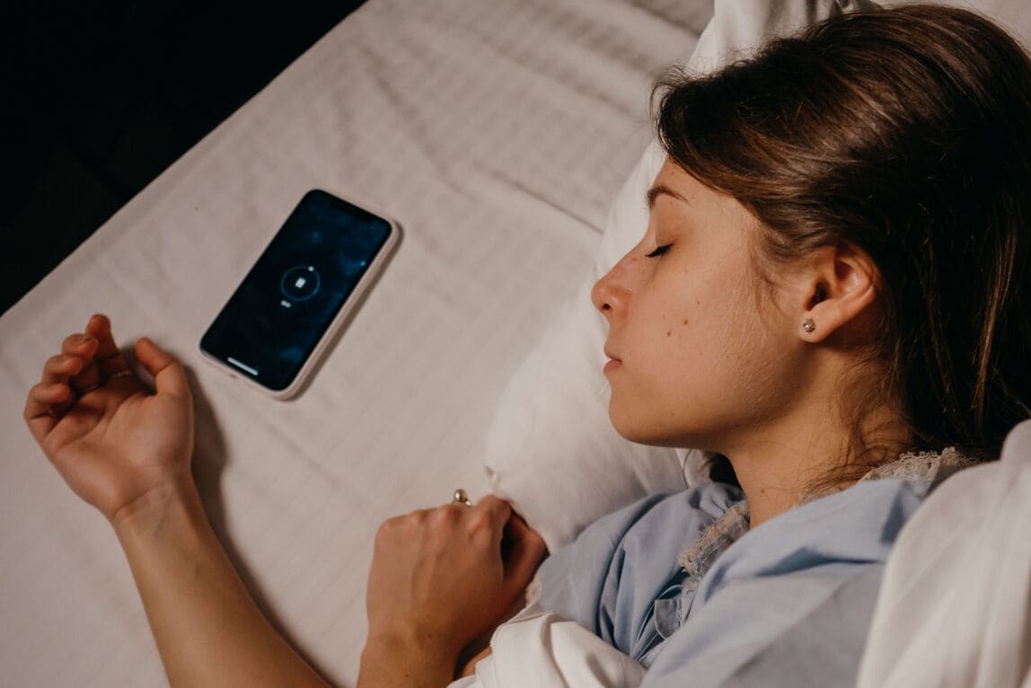 A phone face-down beside a child's bed, playing continuous calm audio like a bedside radio.